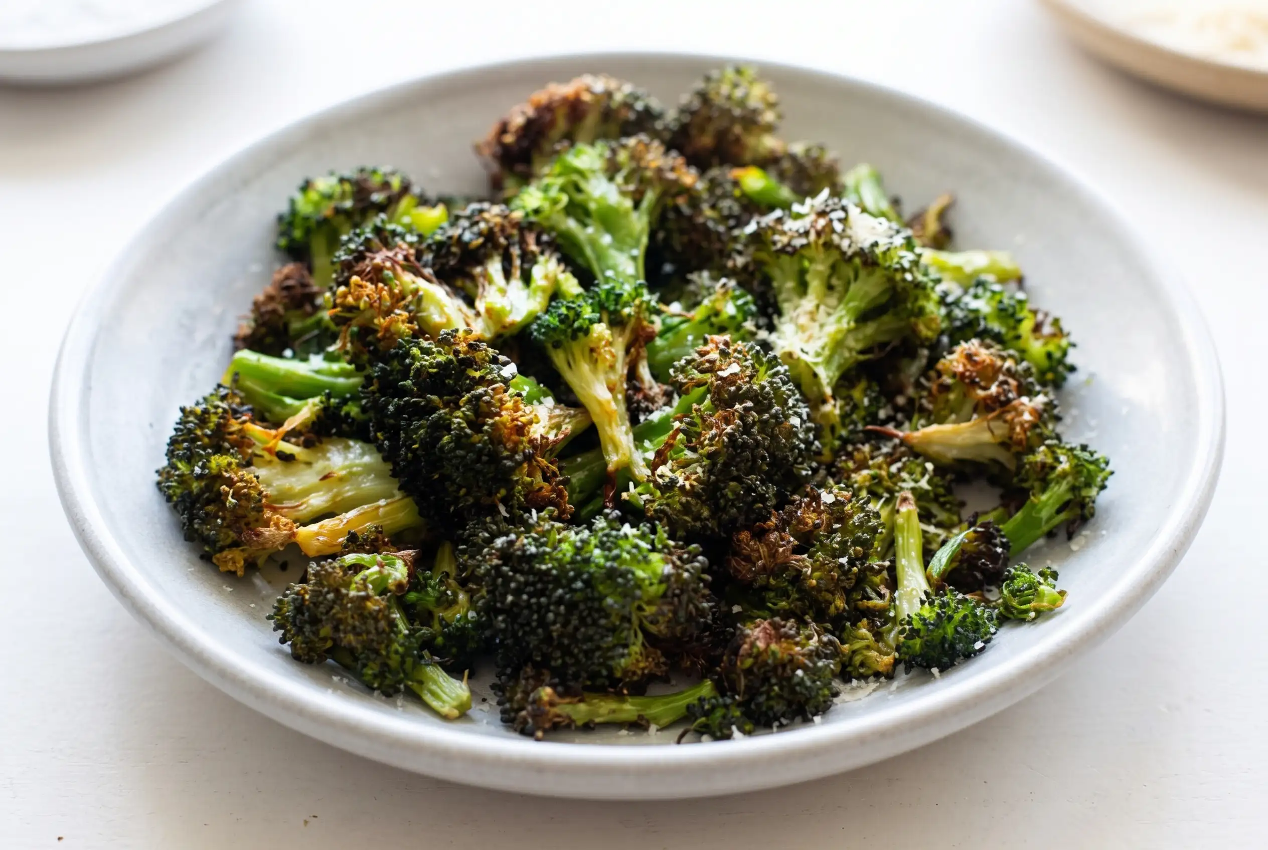Air fryer broccoli with tender green centers and crisp roasted edges in a ceramic serving dish
