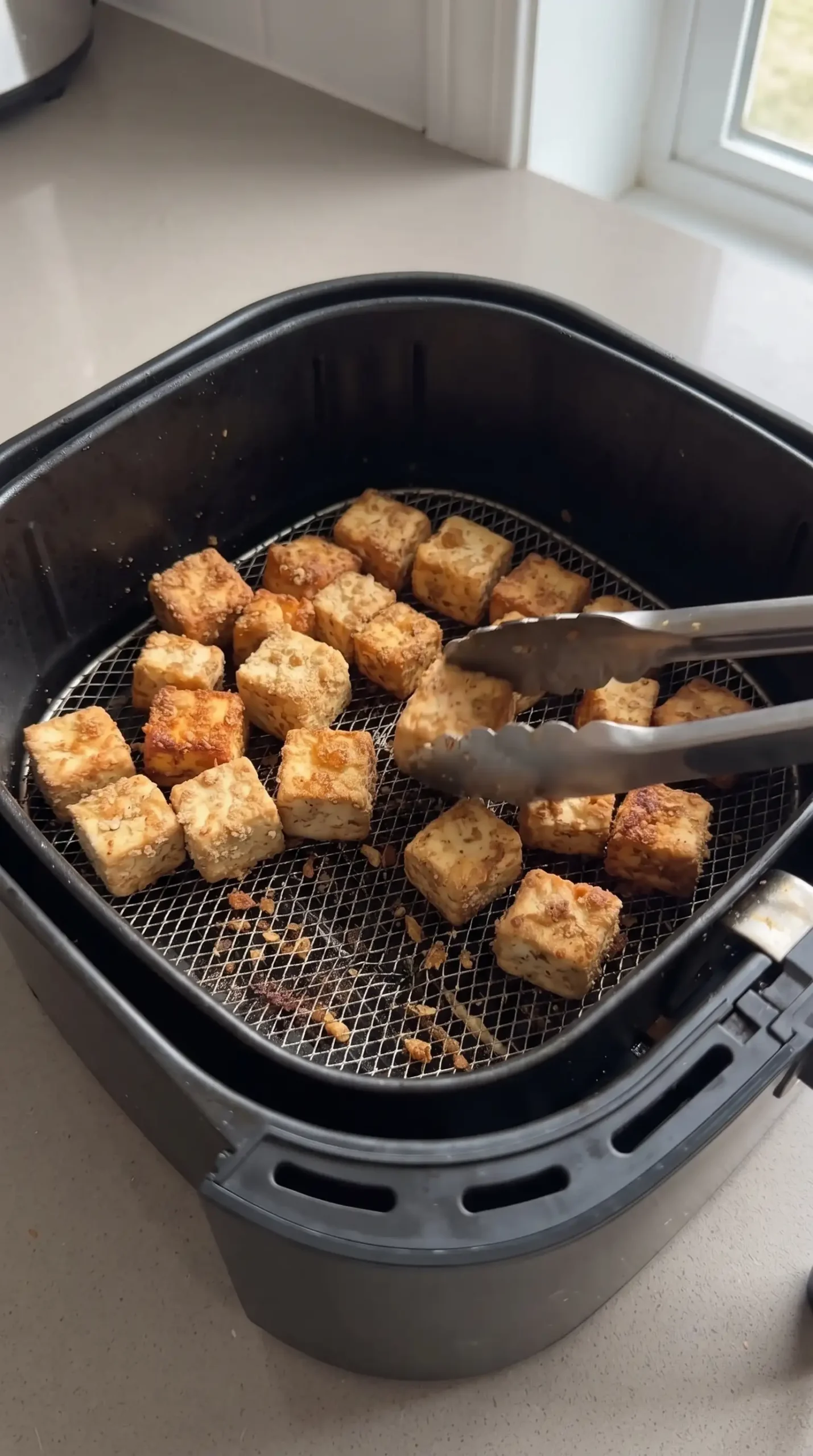 Seasoned tofu chunks crisping in an air fryer for bang bang tofu