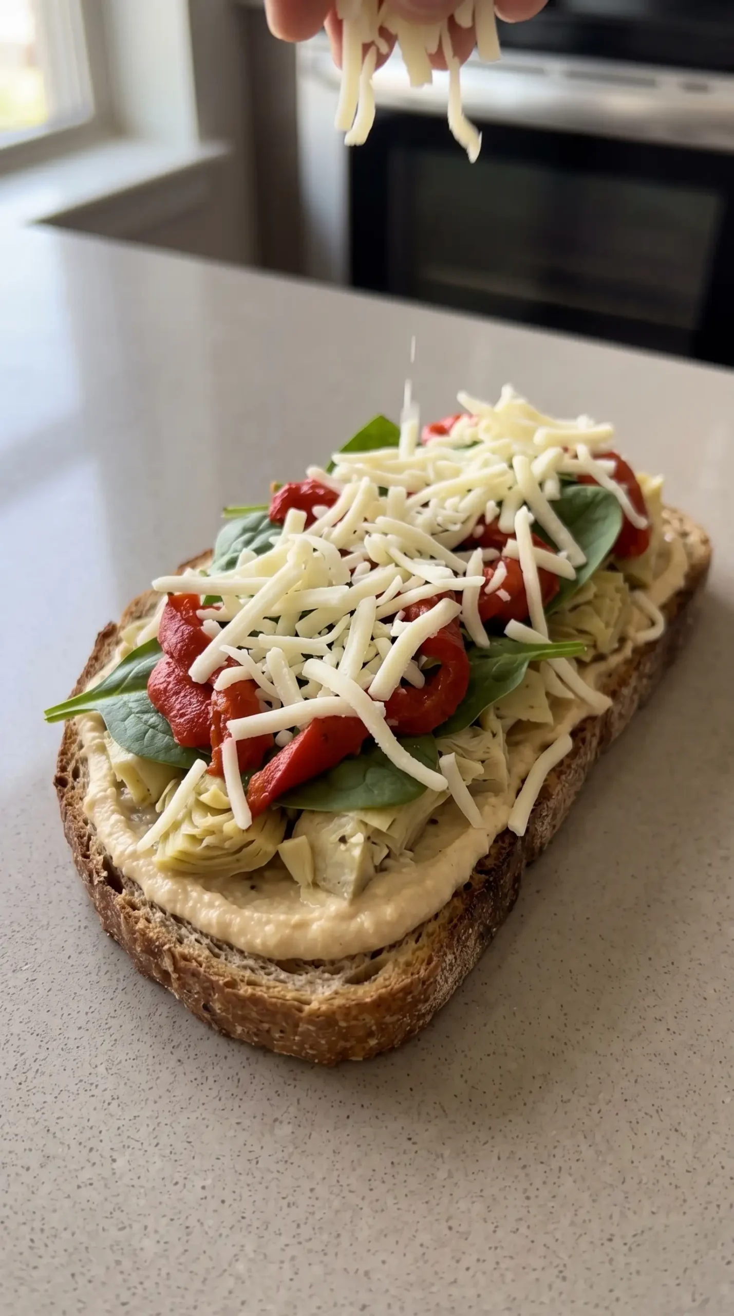 Mozzarella scattered over hummus, vegetables, and bread before baking the melt