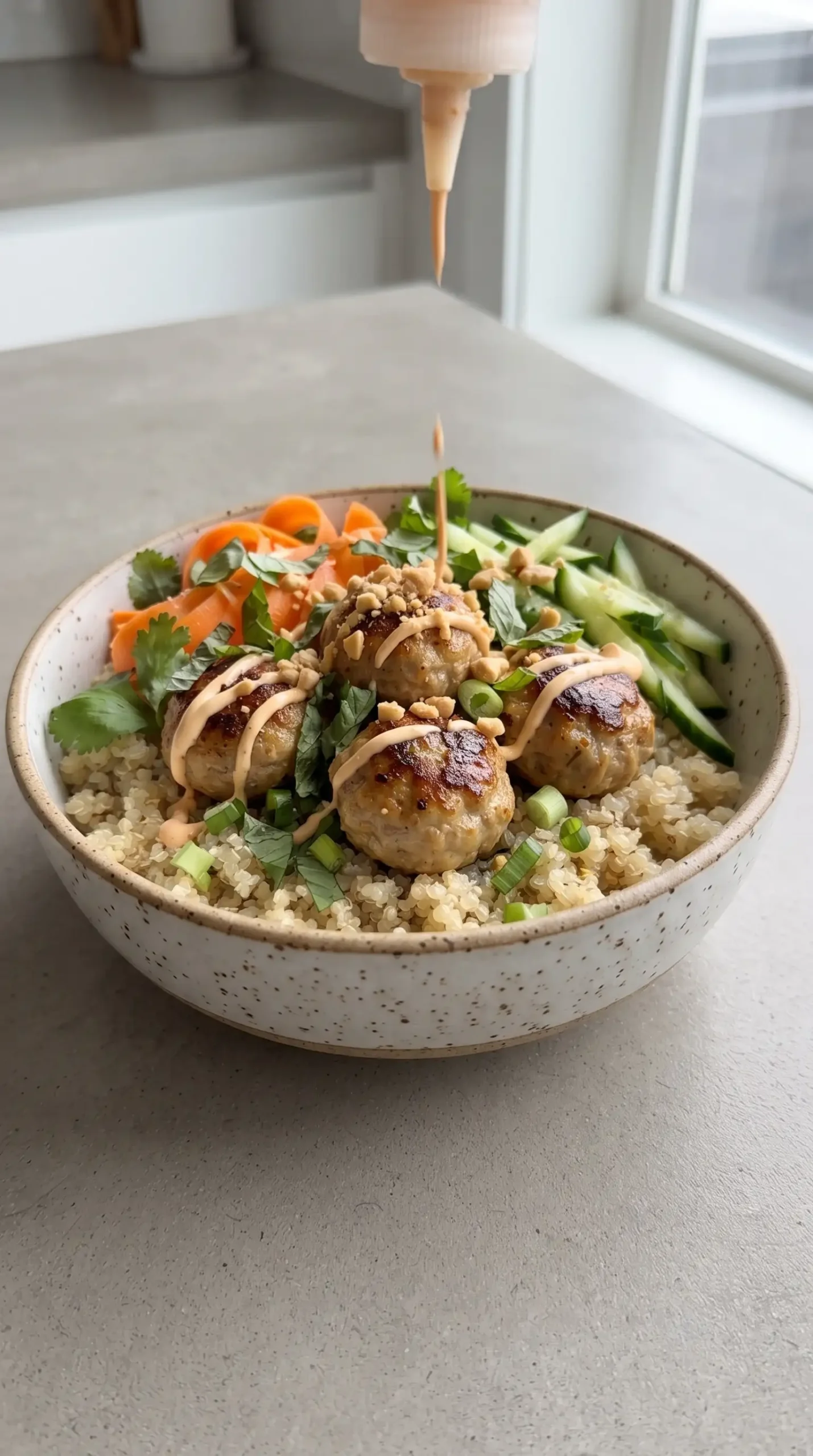 Lemongrass meatball bowl being assembled with quinoa, herbs, carrots, and spicy mayo