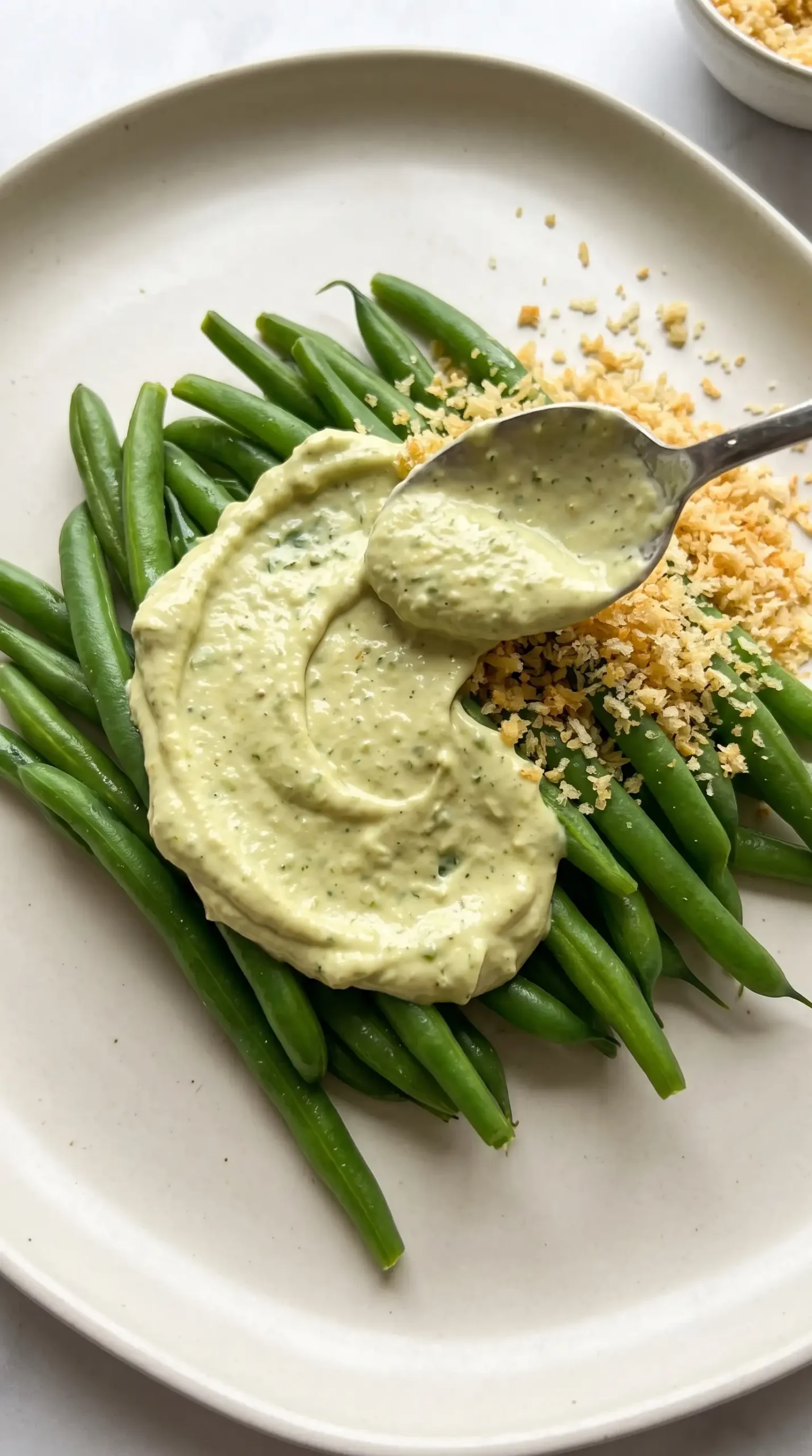 Green beans being coated with avocado Caesar dressing and topped with panko