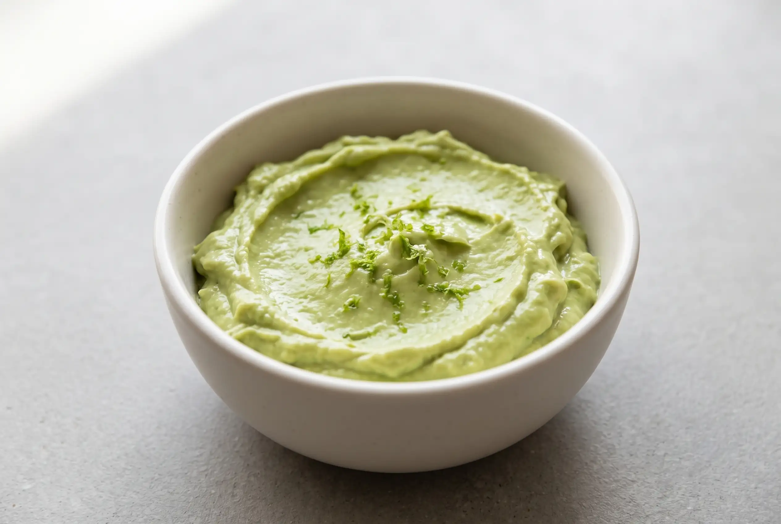 Creamy avocado dip with Greek yogurt served in a small bowl with a smooth pale-green texture
