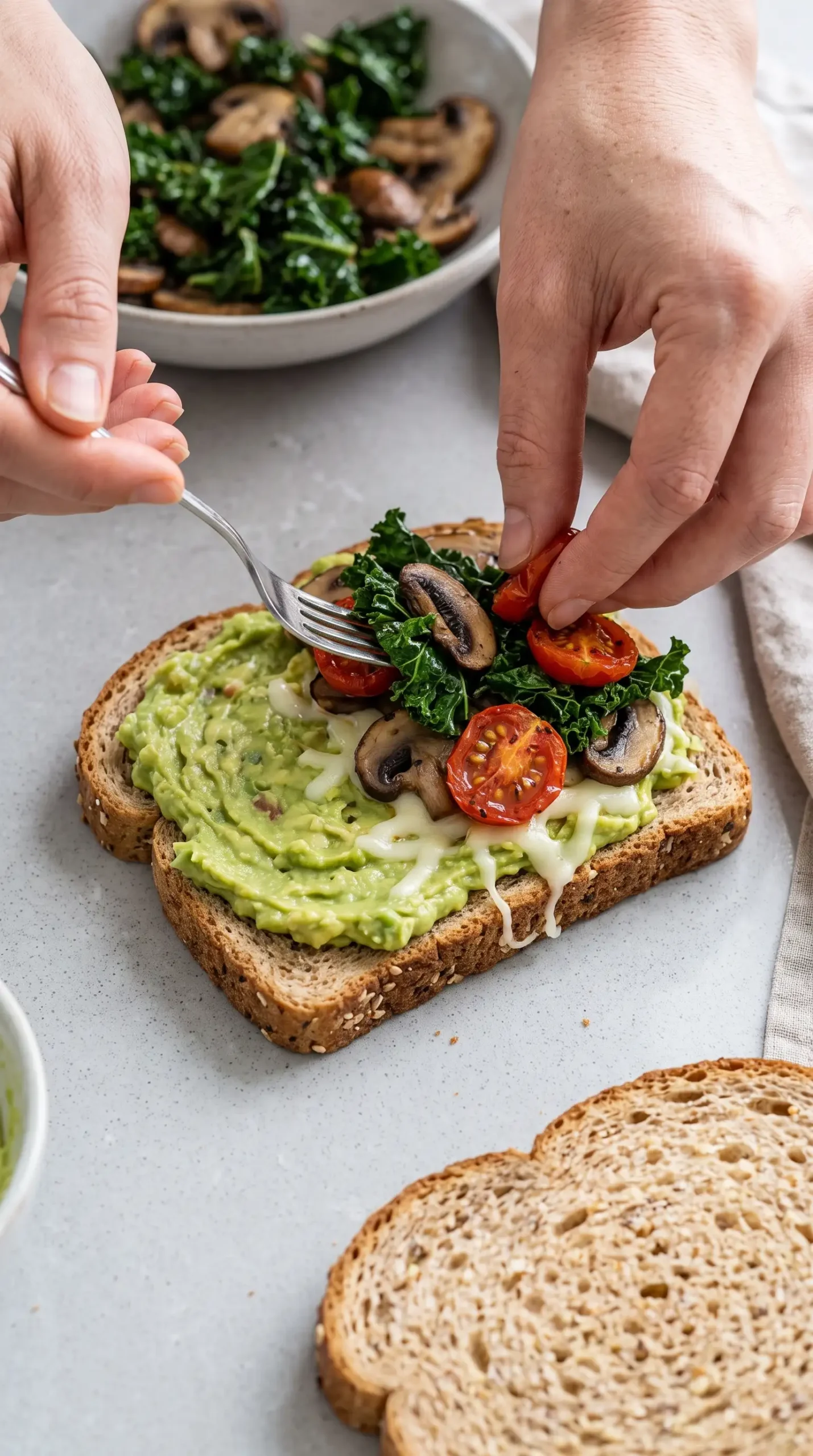 Bread slice spread with avocado and layered with mushrooms, kale, tomatoes, and cheese