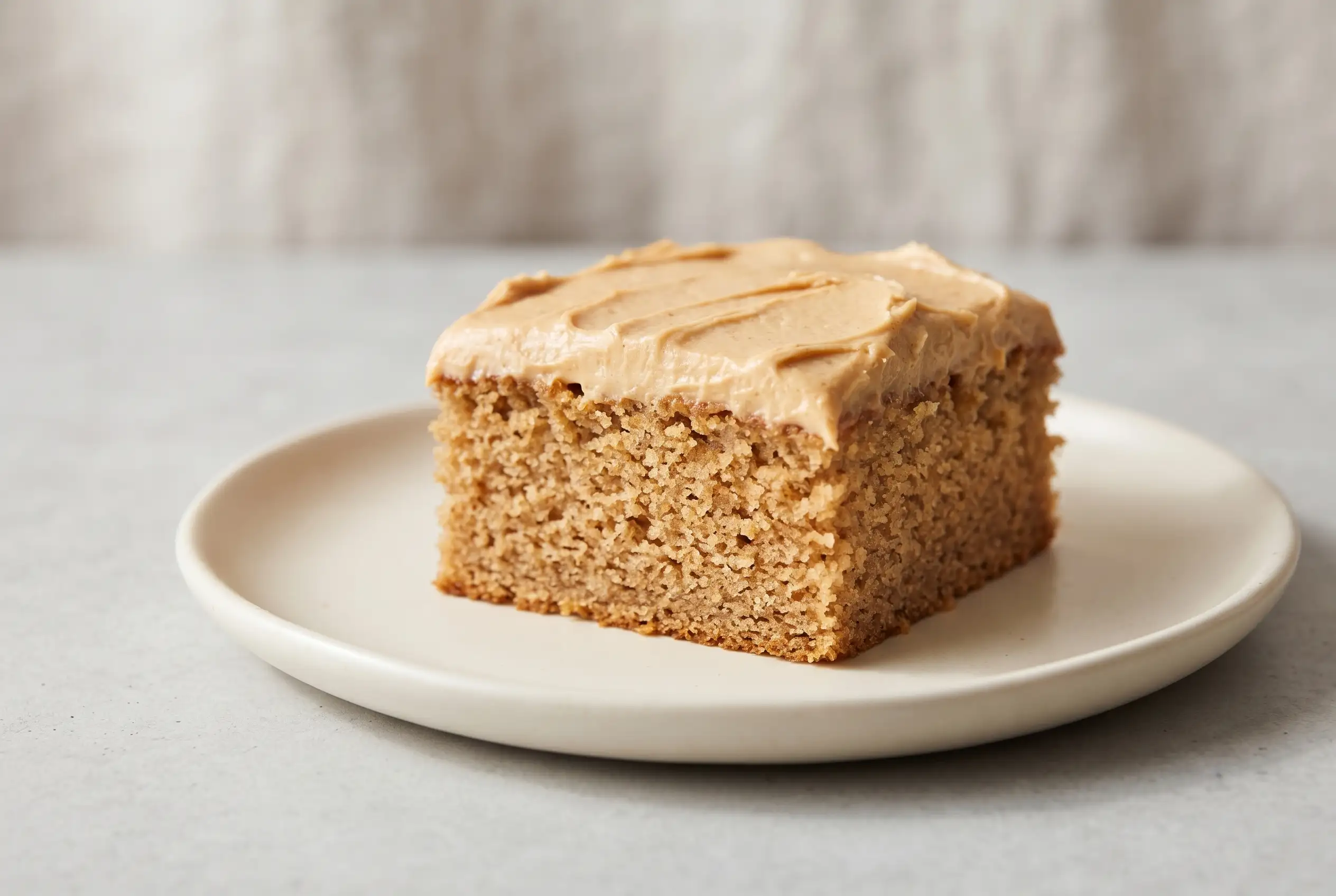 Slice of banana cake with smooth peanut butter frosting on a ceramic plate