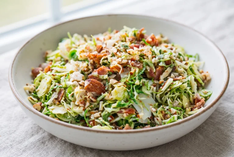 Brussels sprout salad with bacon, Parmesan, almonds, and citrus dressing in a ceramic bowl
