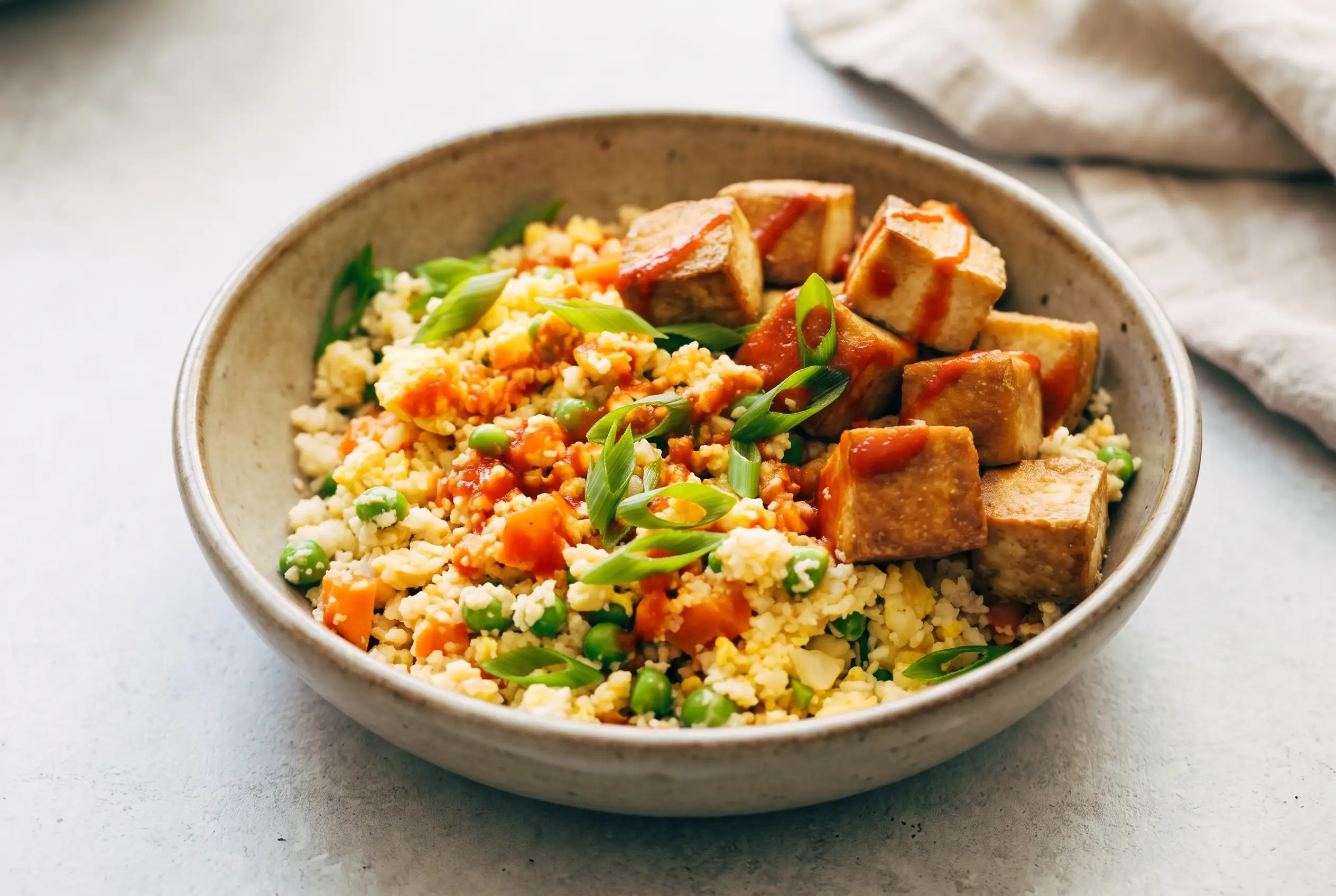Cauliflower fried rice with crispy tofu, vegetables, scrambled eggs, and green onions in a bowl