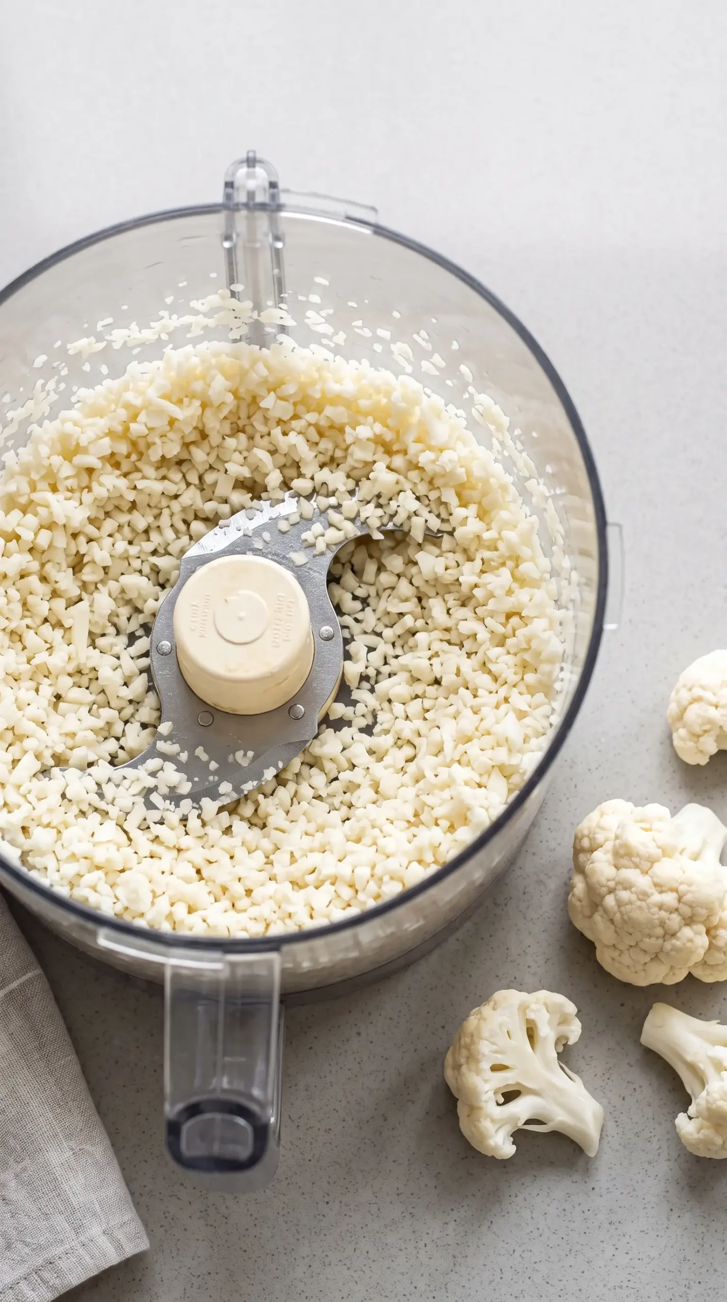 Cauliflower processed into rice-like pieces in a food processor bowl