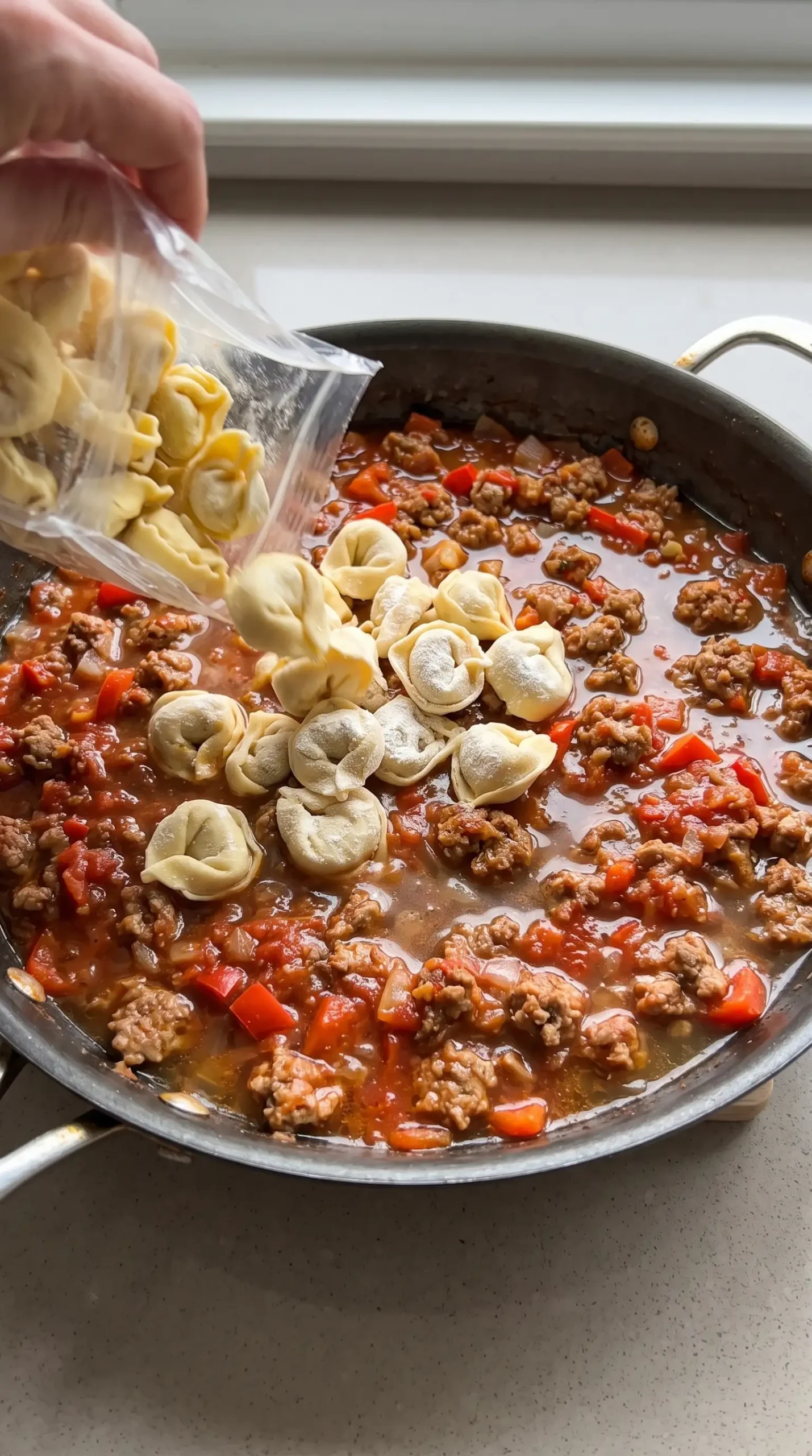 Cheese tortellini added to tomato sauce with sausage in an oven-safe skillet