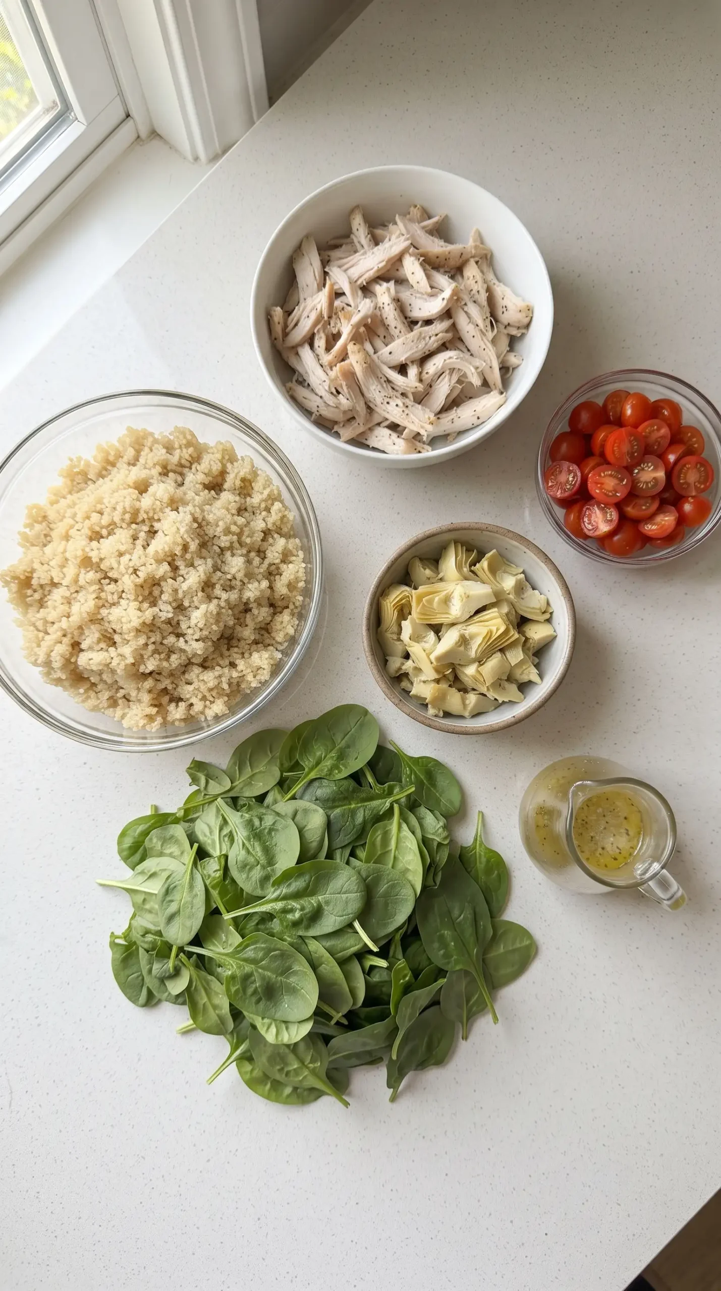 Prepared quinoa, rotisserie chicken, artichokes, tomatoes, spinach, and vinaigrette for salad