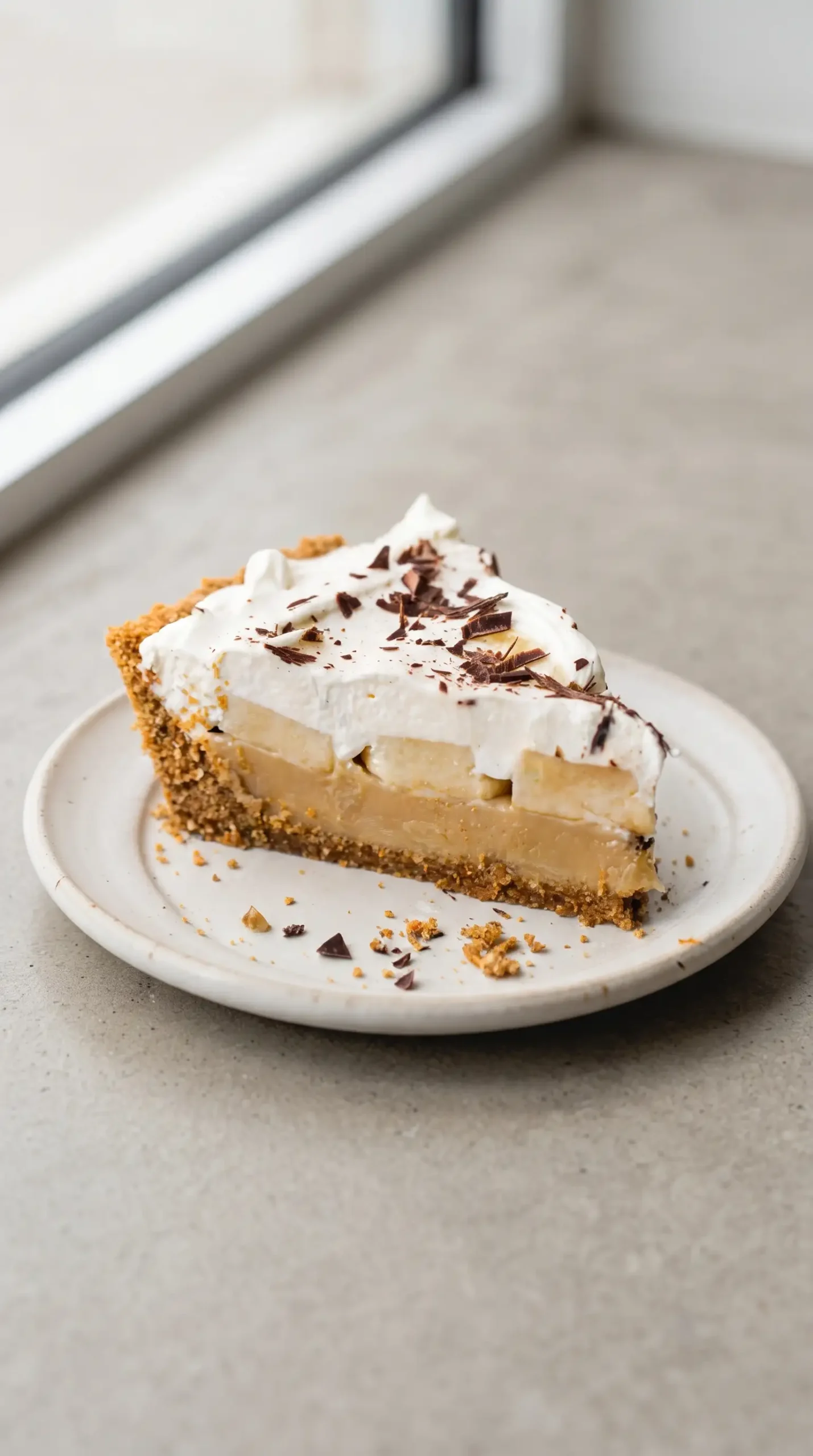 Finished slice of banoffee pie with layers of crust, toffee, bananas, cream, and chocolate