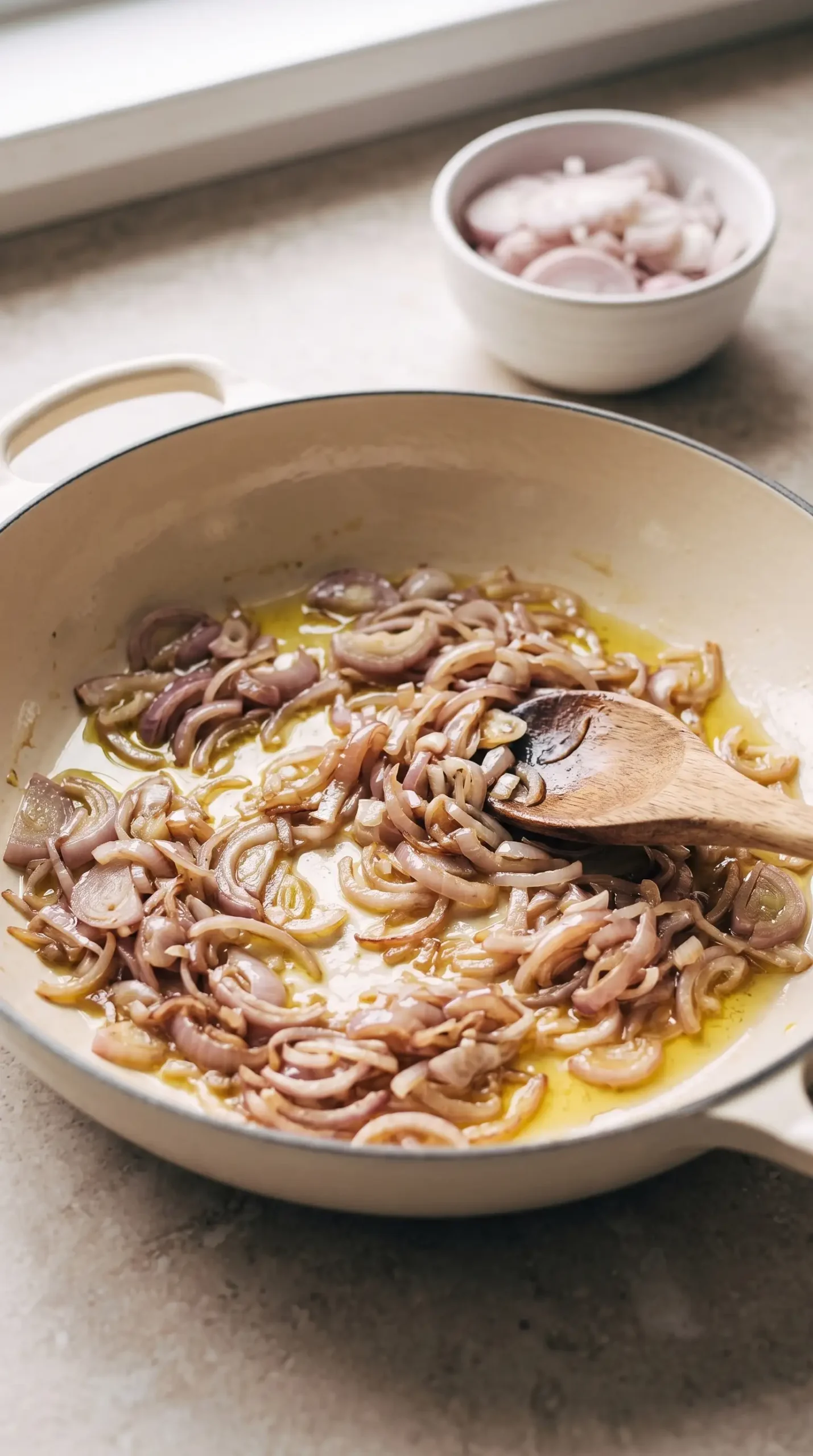 Sliced shallots softening in olive oil until translucent with lightly golden edges.