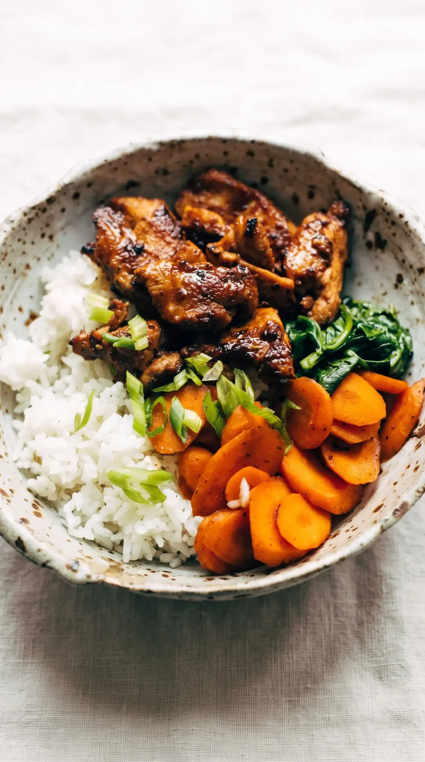 Spicy pork served with rice, carrots, spinach, and sliced green onions